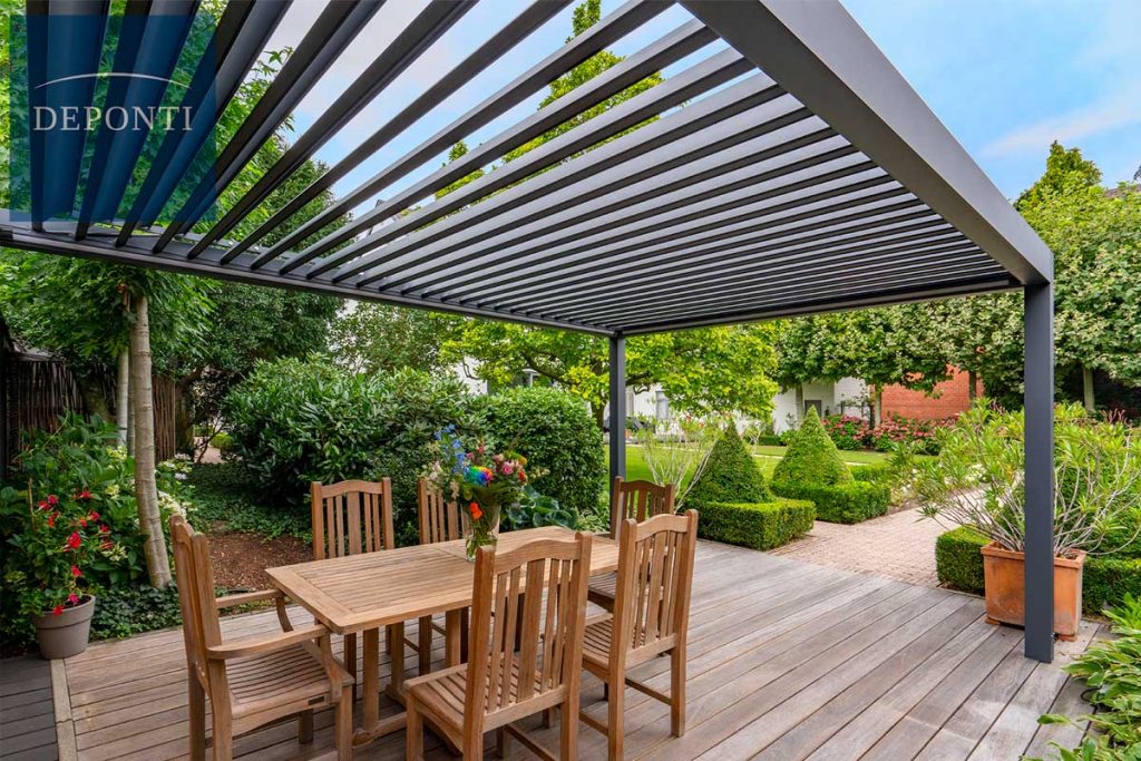 A metal pergola is positioned over a decking area with wooden garden furniture sitting underneath. 