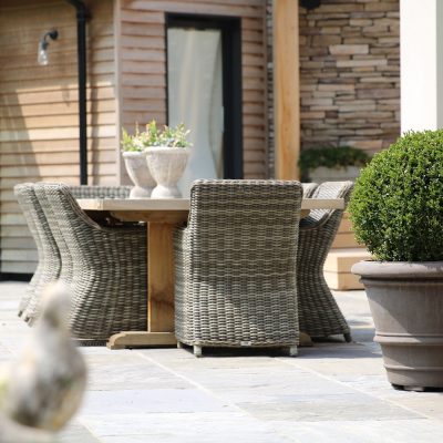 Trimmed shrub in pot on Black tumbled Indian sandstone paving with outdoor furniture with french doors in background.