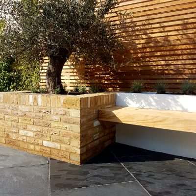 Cantilevered bench on rendered wall next to raised tree pit faced with outdoor wall cladding of facing bricks.