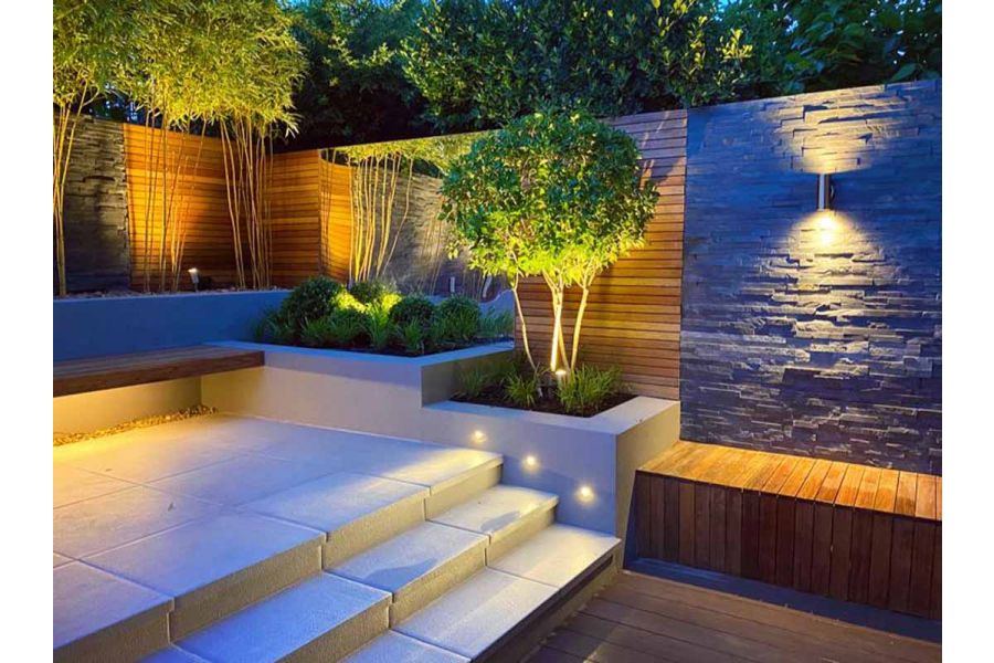 Black slate stone cladding panels lit with up and down lighters, next to raised beds and steps. Design by Tom Howard. 