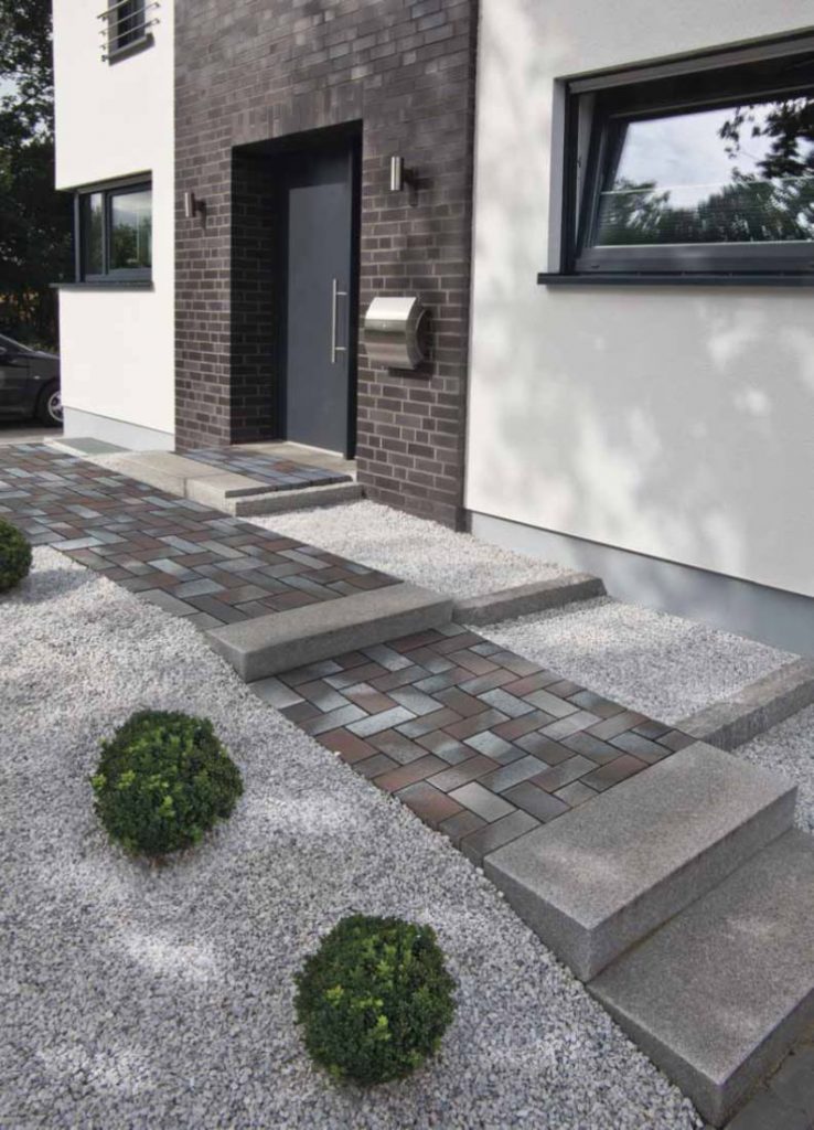 Path of Delta Blue Brown clay paving with steps runs parallel to modern building with white walls and brick entrance.