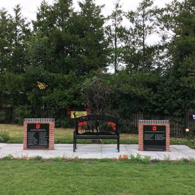 2 black plaques on brick monuments flanking black metal bench, Sandiway and Cuddington War Memorial, by Amazing Garden Design.
