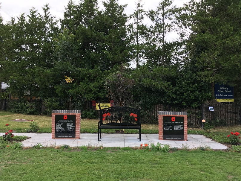 2 black plaques on brick monuments flanking black metal bench, Sandiway and Cuddington War Memorial, by Amazing Garden Design.
