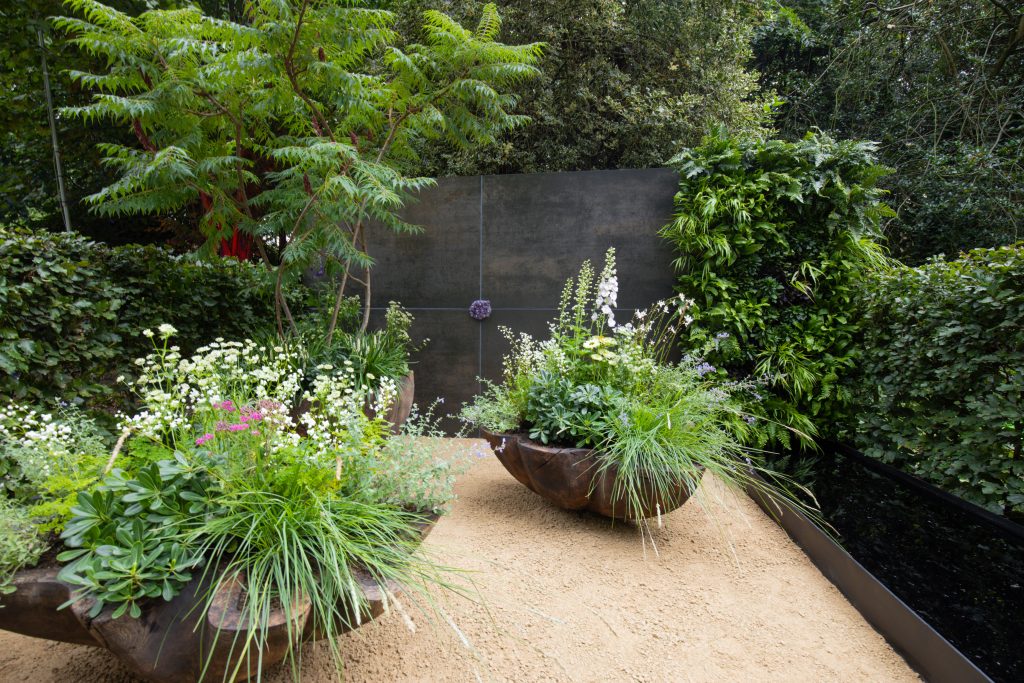 Steel Dark Luxury DesignClad makes a statement as the backdrop to lush planting in this container garden. 