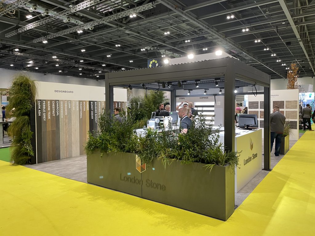 A metal pergola covers the desk. Throughout the display composite decking, porcelain and natural stone paving can be seen. 