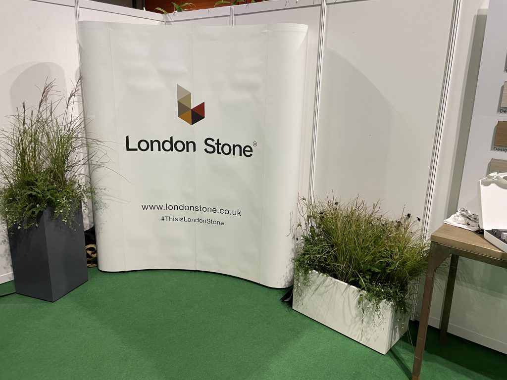 London Stone sign with fibreglass planters either side filled with perennial plants.