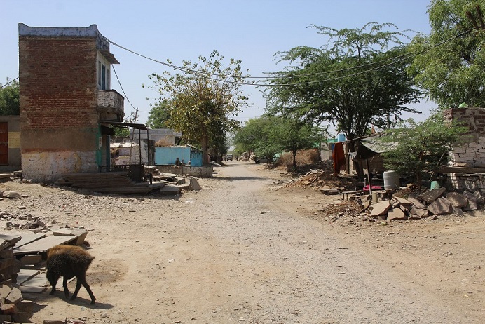 Dusty lane between trees and small houses and shacks, Budhpura, Rajasthan, India