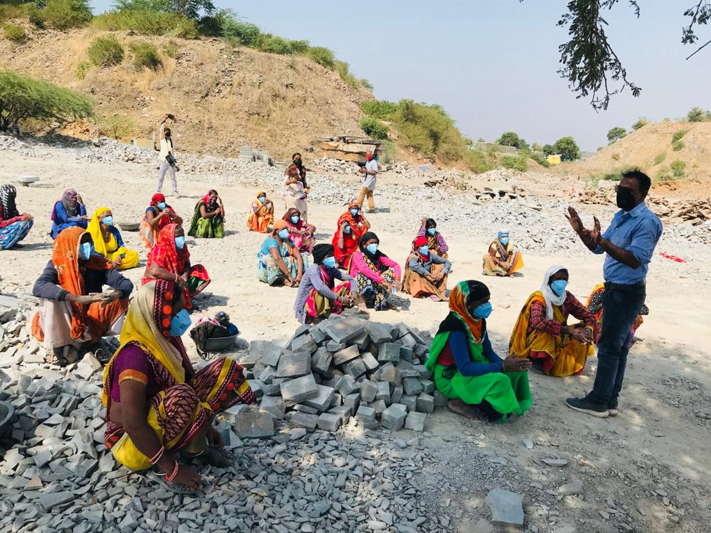 Group of well spaced women sitting on ground, Budhpura, India, receiving training in Covid safety.