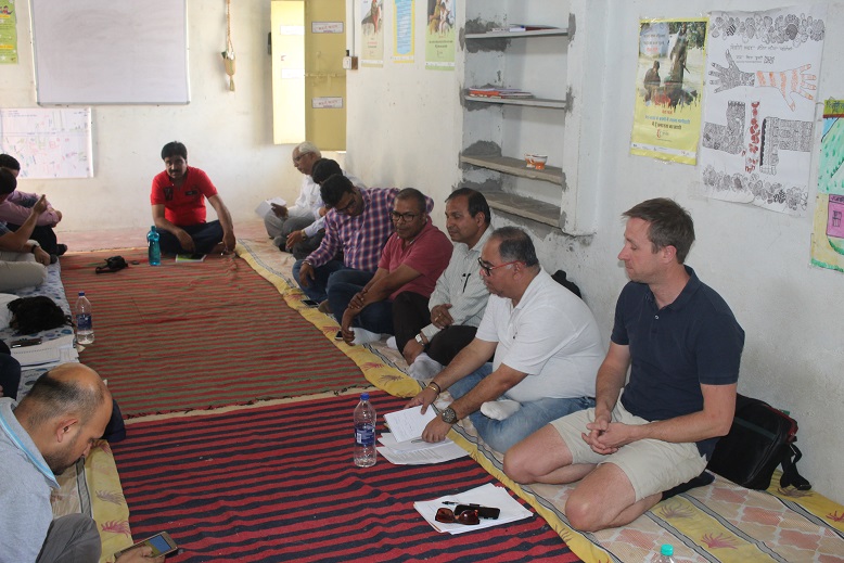 Line of men sitting on floor along wall of room, in meeting about ethical sourcing, Budhpura, Rajasthan, India