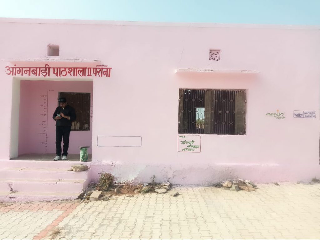 Pink-washed, single-storey building, an Early Childhood Care and Development Centre with man standing in doorway