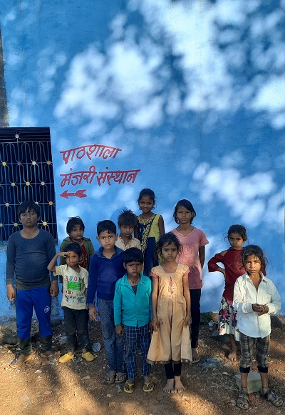 Group of children standing in front of blue-walled building with red writing that says Manjari Learning Space in Indian script.