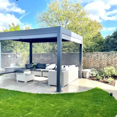 Dark grey metal pergola, 2 sides lowered, over oval patio with curved path leading away.,