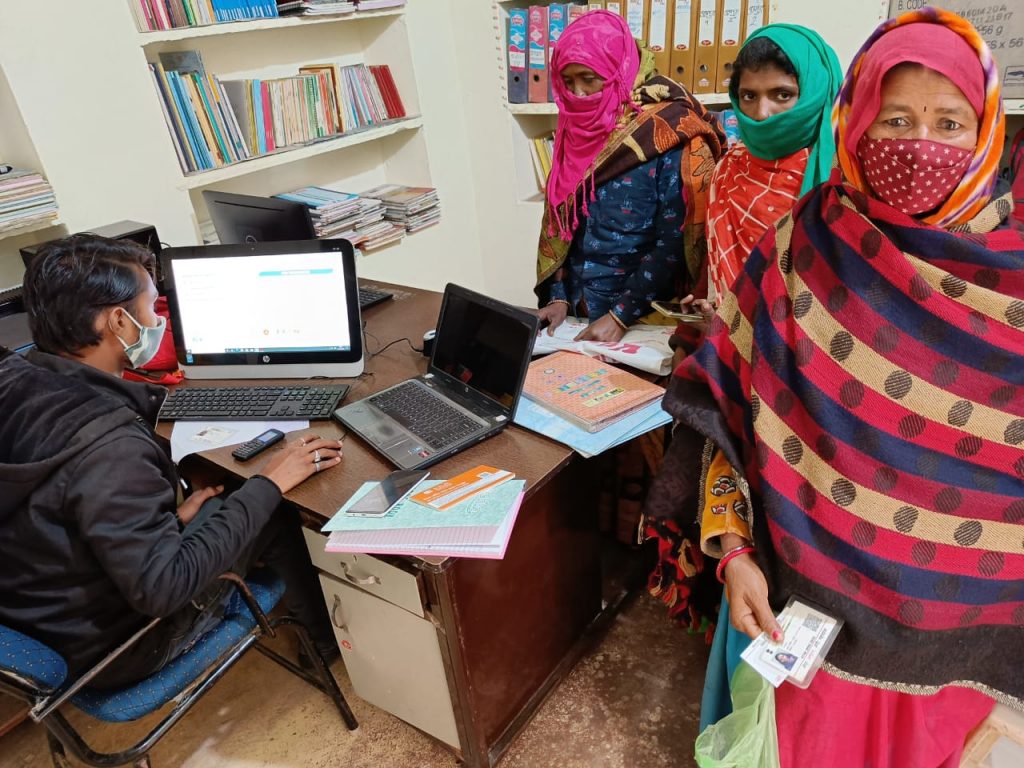 Man sits at computer, registering Indian women workers for their E-Shram card.