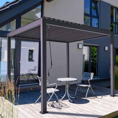 Grey Proteus 4m x 3m rectangular pergola with louvered roof on decking patio with white bistro set.