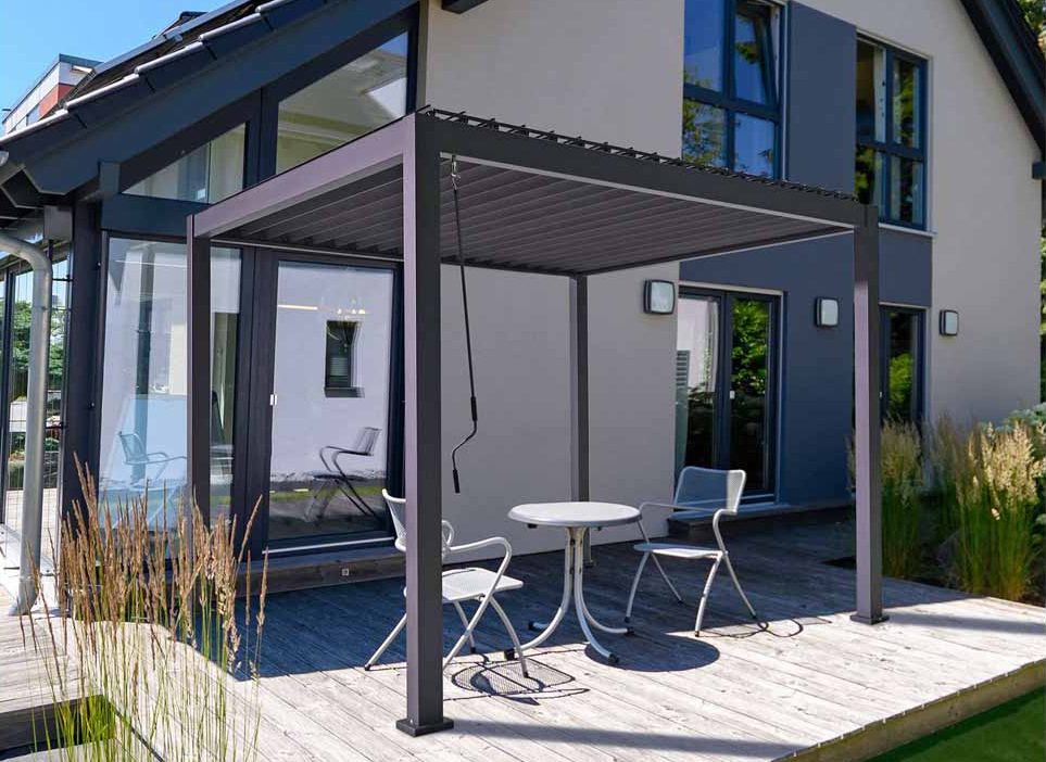 Grey Proteus 4m x 3m rectangular pergola with louvered roof on decking patio with white bistro set.