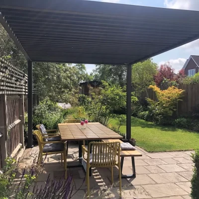 Proteus Grey 3x4 aluminium pergola over wooden furniture on natural stone patio looking out to lawned garden.