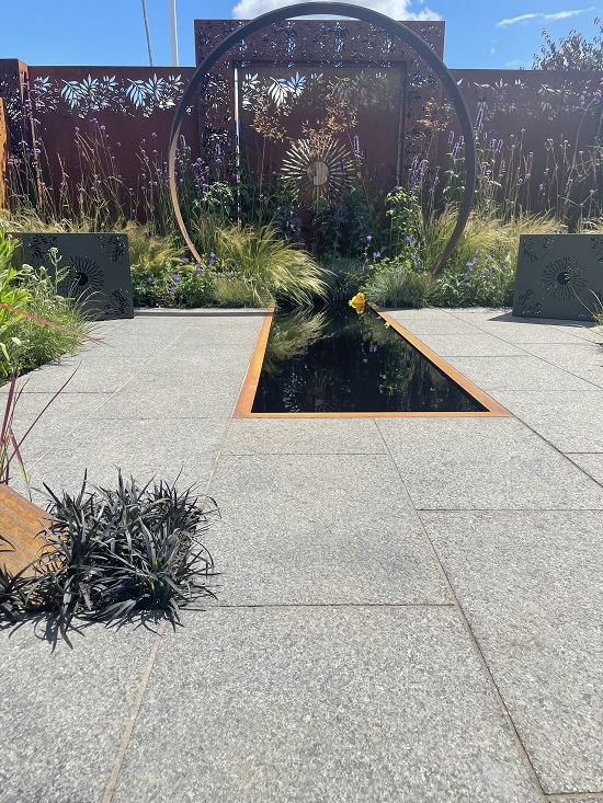 Corten Steel moongate and Dark Grey Granite Paving in Sunburst garden, RHS Hampton Court 2022, by Charlie Bloom and Simon Webster.