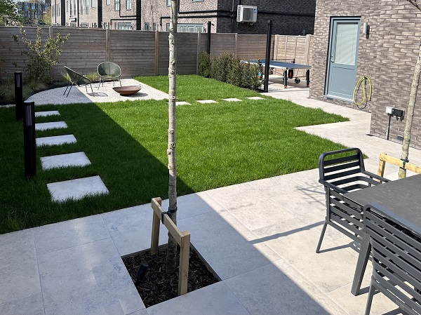 Garden with Jura Grey limestone porcelain paving used for patio, paths and stepping stones in lawn to gravel fire pit area.