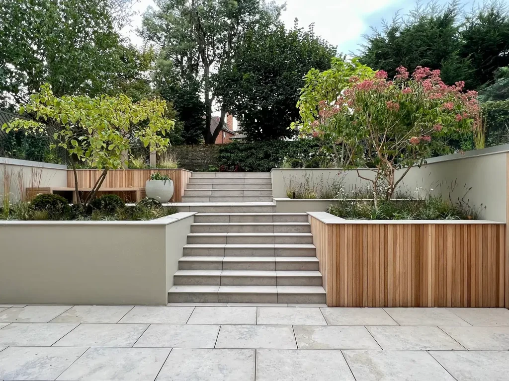 Jura Grey porcelain steps, flanked by deep beds with trees,  rise in 2 consecutive flights from paving to upper garden level.