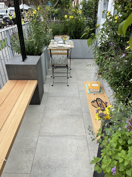 Light grey porcelain paving on Landform Balcony garden at RHS Chelsea 2021, with wooden bench and bistro set.