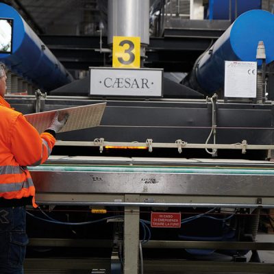 Man in hi-vis jacket stands by conveyor belt in Italian factory, showing how are porcelain tiles made