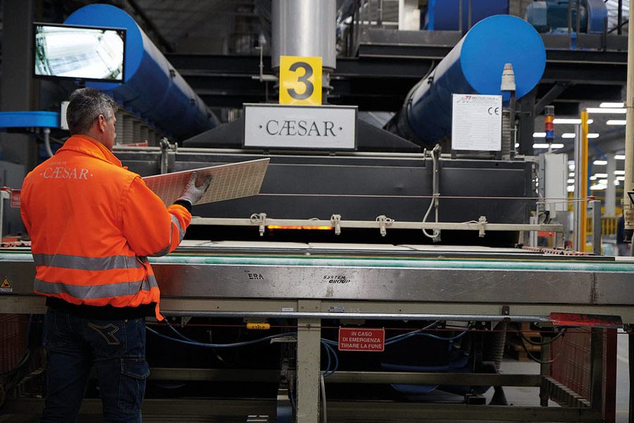 Man in hi-vis jacket stands by conveyor belt in Italian factory, showing how are porcelain tiles made