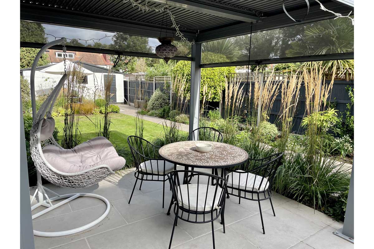 Florence Grey Porcelain pavers with garden furniture under pergola. Design by Emily's Gardens, built by JR Landscaping