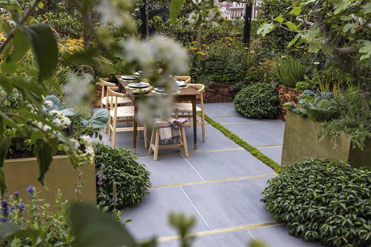 The Parsley Box show garden with Sidewalk Porcelain extra-large patio paving, raised beds and dining set.