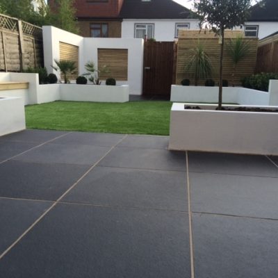 Midnight Black limestone patio paving with blocky white raised beds and wooden seating and screens. Design by Lifestyle Gardens.