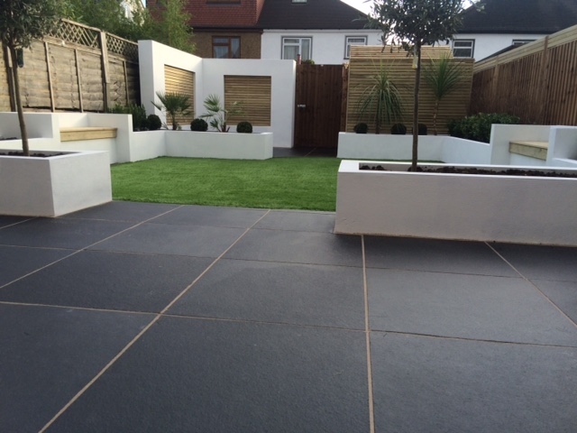 Midnight Black limestone patio paving with blocky white raised beds and wooden seating and screens. Design by Lifestyle Gardens.
