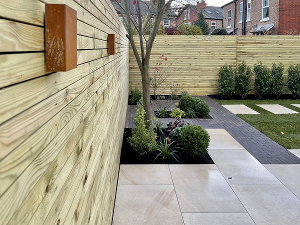 Ash Beige porcelain garden tiles and Amersham clay pavers with inset beds next to slatted fence.