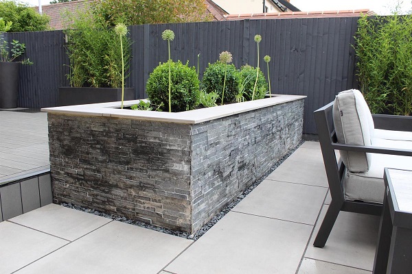 Polished concrete porcelain garden tiles with matching coping on raised bed faced with slate cladding.