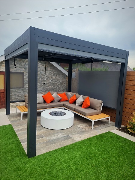 Dark Grey aluminium pergola over area paved with porcelain planks with modular sofa and firepit. Built by Stonecraft, Lancashire.