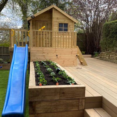 Warm teak composite decking with large Wendy house and raised wooden vegetable bed.