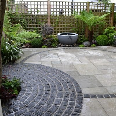 Kandla Grey Indian Sandstone combined with curves of granite setts in fenced garden with water bowl feature.