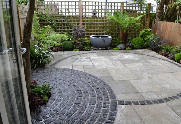 Kandla Grey Indian Sandstone combined with curves of granite setts in fenced garden with water bowl feature.