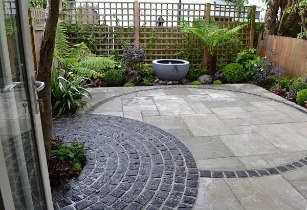 Kandla Grey Indian Sandstone combined with curves of granite setts in fenced garden with water bowl feature. 