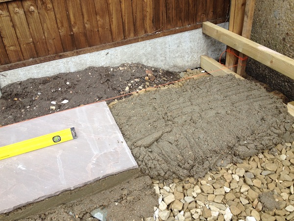 Indian sandstone slab with spirit level lies on full bed of mortar on aggregate sub base next to string line.