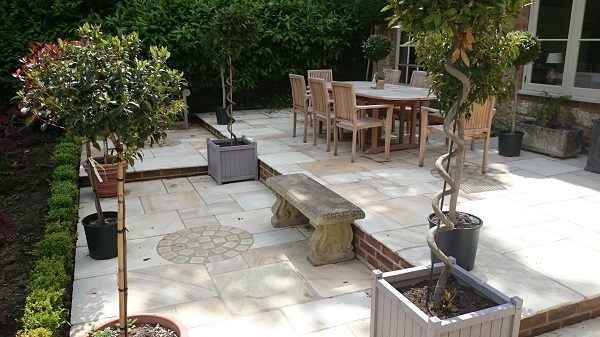 Mint sandstone tumbled paving on 3 levels with large wooden dining set, wooden planters and stone bench.