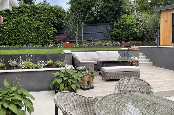 Cinnamon DesignBoard composite decking with rattan furniture, grey rendered walls and steps to raised lawn.