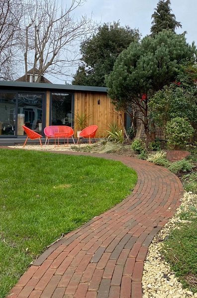 Curved garden path in Winton brick pavers leads to studio with furniture outside.