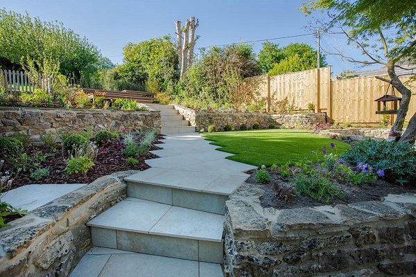 Gea porcelain steps rise to garden path past lawn to raised terrace.