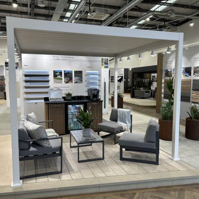 Indoor display with white pergola, furniture, coffee machine and wall displays of hard landscaping materials.
