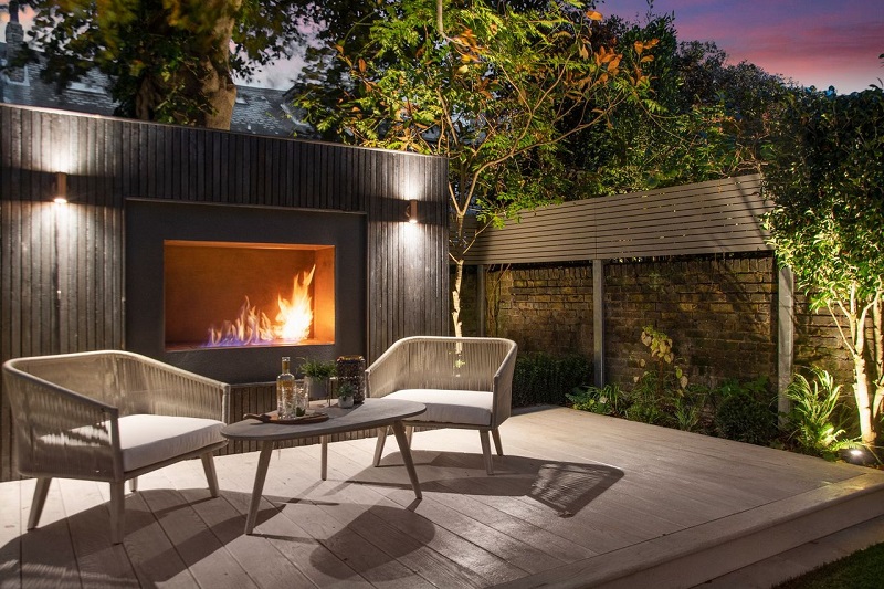 Outdoor fireplace framed in DeslgnClad Steel Corten with 2 chairs and table on decking.