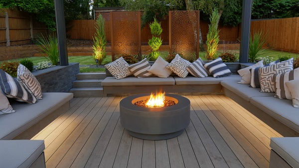 Round fire pit on DesignBoard traditional decking in centre of square sunken seating pit with cushions. Design by Landscapia
