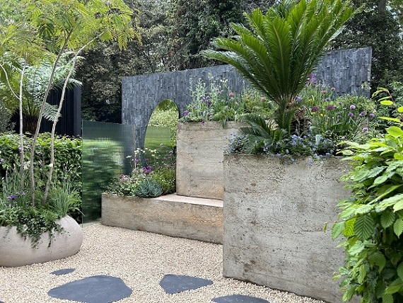 Large hypertufa container against black slate cladding wall with tall, curve-edged mirror. The Shifting Garden, Chelsea Gardener