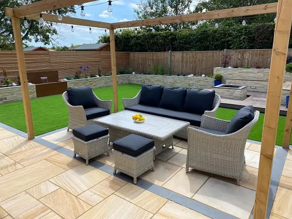 Dune sandstone patio with blue granite planks under wood pergola strung with lights.