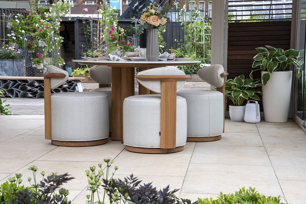 Round cream and wood stools at table on Jura Beige porcelain paving. Mauve flowers in foreground.