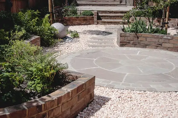 Paving circle set in gravel edged with curved raised beds shows colour of Indian sandstone Kandla Grey