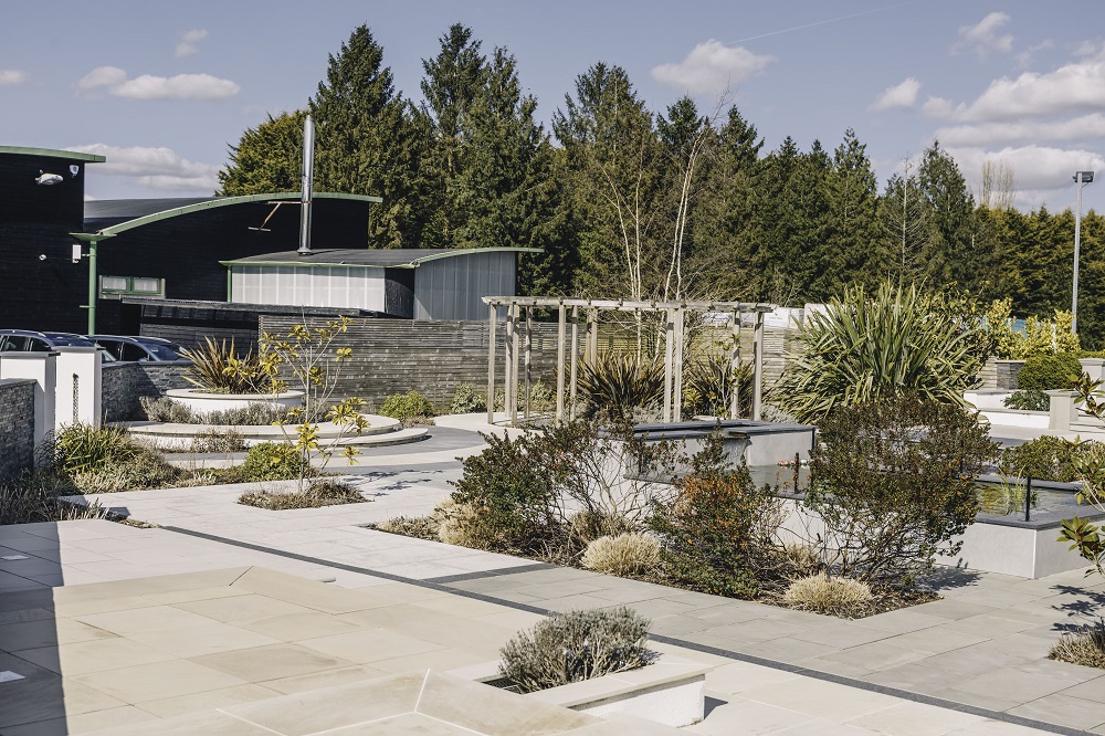 View across Kent showroom's external paving display of sandstone, with pergola and planting